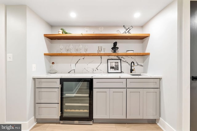 bar featuring beverage cooler, gray cabinets, light stone counters, and sink