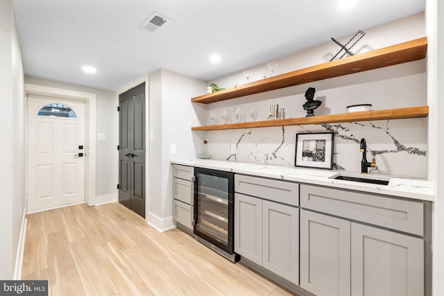 bar with sink, gray cabinetry, beverage cooler, light hardwood / wood-style flooring, and light stone countertops