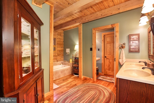 bathroom with beam ceiling, a relaxing tiled tub, hardwood / wood-style flooring, and wooden ceiling