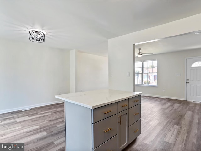 kitchen with a center island, light wood-type flooring, light stone countertops, gray cabinets, and ceiling fan