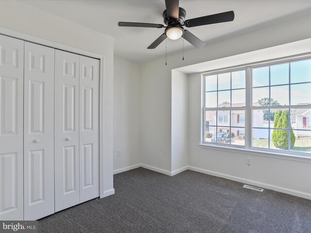 unfurnished bedroom with a closet, ceiling fan, and dark colored carpet