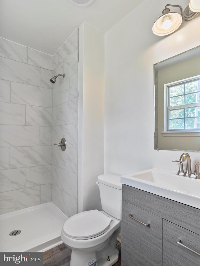 full bath featuring a tile shower, toilet, vanity, and wood finished floors