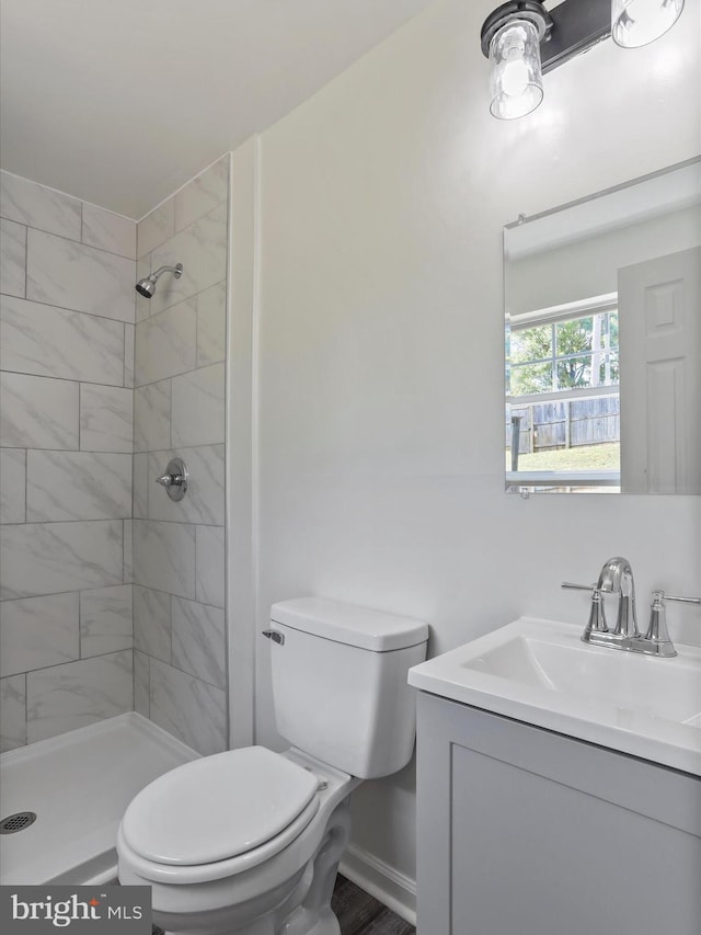 bathroom with toilet, a tile shower, and vanity