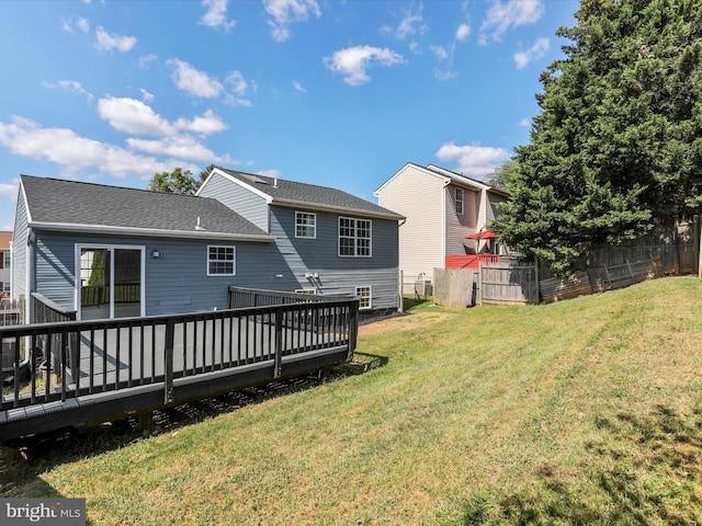 rear view of property featuring a wooden deck, a lawn, a shingled roof, and fence