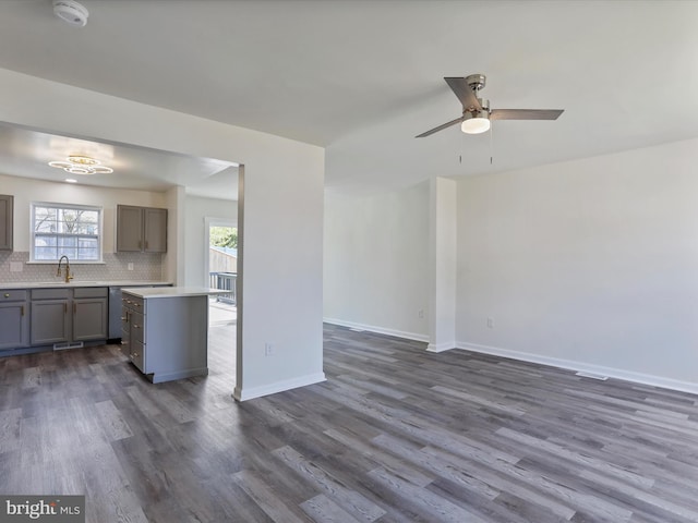 unfurnished living room with dark wood finished floors, a ceiling fan, baseboards, and a sink