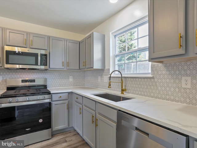 kitchen with gray cabinetry, light wood-type flooring, light stone countertops, stainless steel appliances, and sink