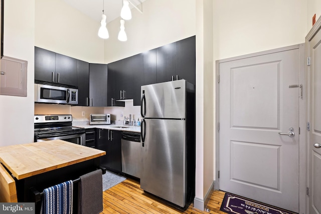 kitchen featuring hanging light fixtures, sink, light hardwood / wood-style flooring, stainless steel appliances, and a towering ceiling