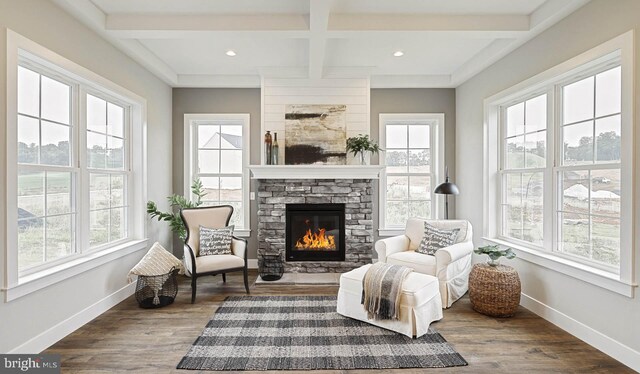 living area featuring beam ceiling, coffered ceiling, dark wood-type flooring, and a stone fireplace