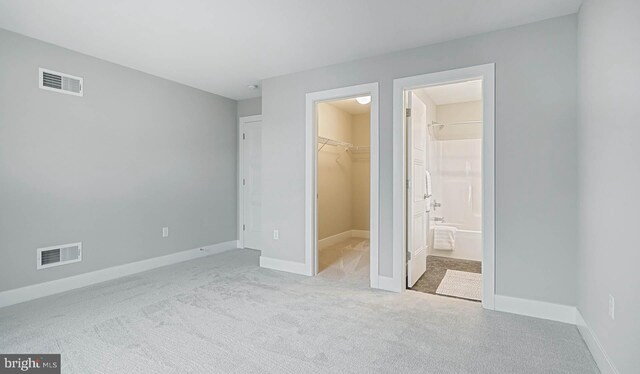 unfurnished bedroom with light colored carpet, ensuite bath, a walk in closet, and a closet