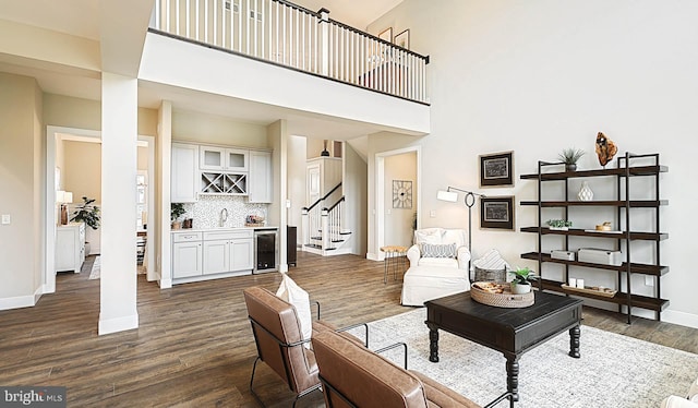 sitting room with beverage cooler, wet bar, a towering ceiling, and dark wood-type flooring