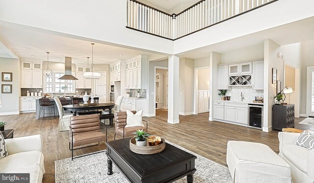 living room with a high ceiling, beverage cooler, indoor bar, and hardwood / wood-style flooring