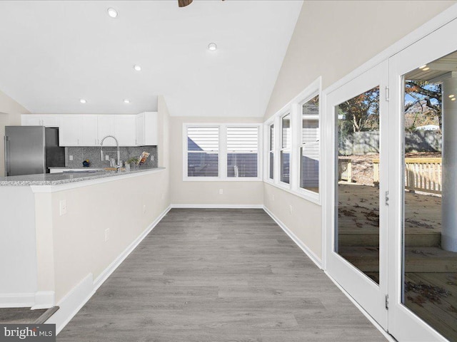 kitchen featuring vaulted ceiling, backsplash, stainless steel refrigerator, white cabinetry, and light wood-type flooring