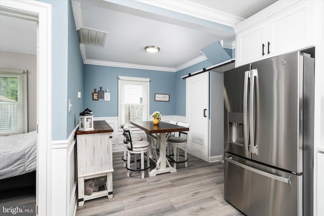 kitchen with white cabinets, stainless steel fridge, ornamental molding, light hardwood / wood-style flooring, and a barn door