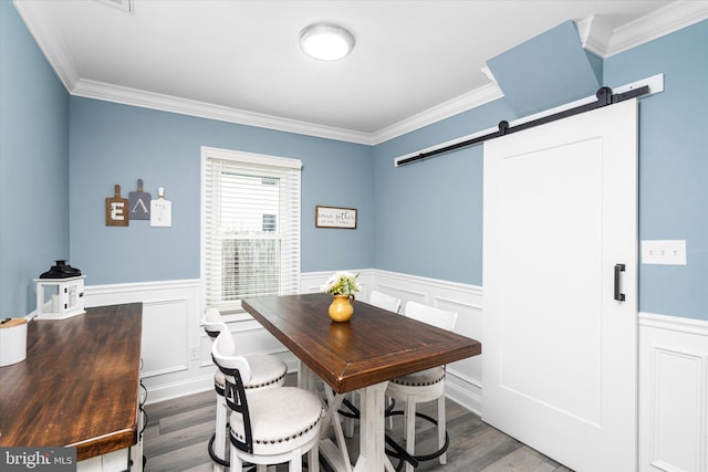 dining area featuring a barn door, ornamental molding, and hardwood / wood-style floors