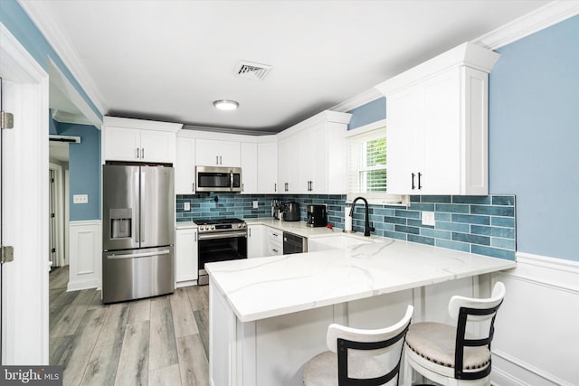 kitchen featuring stainless steel appliances, white cabinets, light stone counters, and light wood-type flooring