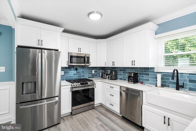 kitchen with white cabinets, ornamental molding, sink, light hardwood / wood-style flooring, and appliances with stainless steel finishes