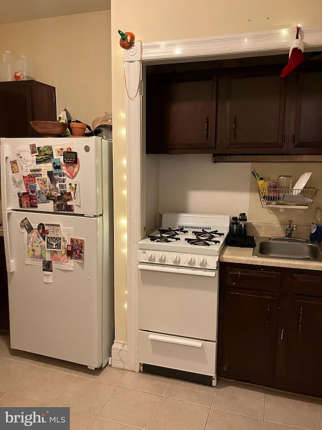 kitchen featuring light tile patterned floors, sink, dark brown cabinetry, and white appliances