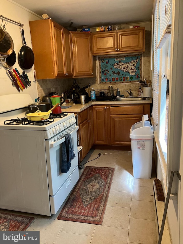 kitchen with backsplash, white gas range, sink, light tile patterned flooring, and ornamental molding