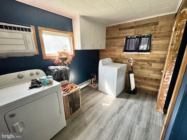 laundry area featuring cabinets, light hardwood / wood-style floors, wood walls, a baseboard radiator, and washing machine and dryer