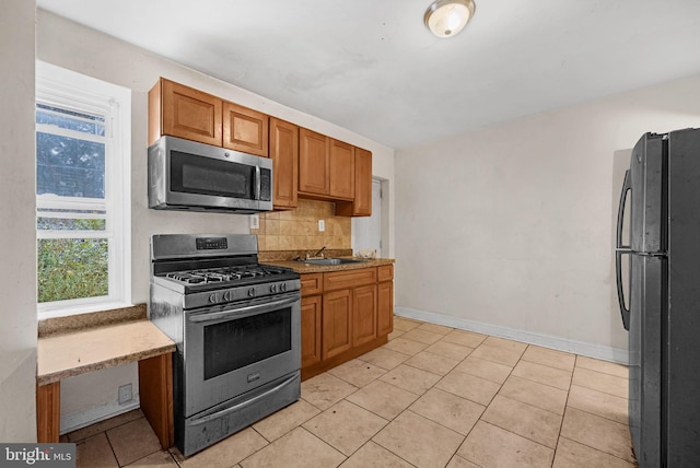 kitchen with light stone countertops, light tile patterned floors, backsplash, appliances with stainless steel finishes, and sink