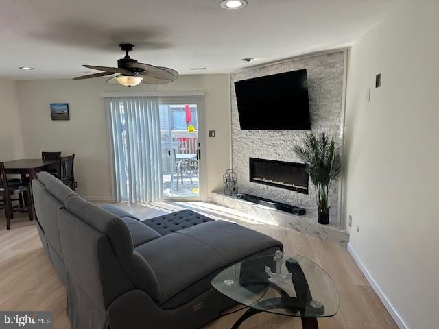 living room featuring ceiling fan, a fireplace, and light wood-type flooring