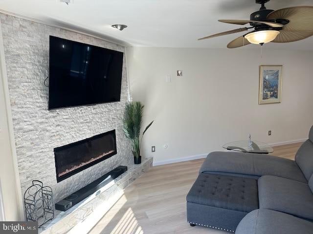 living room with light hardwood / wood-style floors, a stone fireplace, and ceiling fan