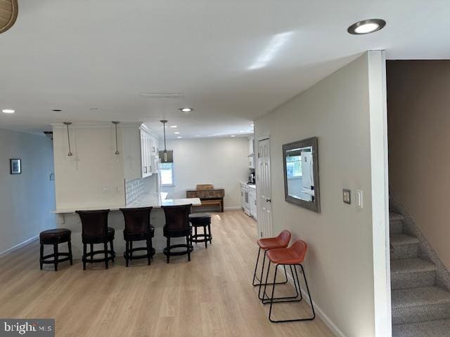 kitchen with a breakfast bar, light hardwood / wood-style floors, white cabinets, kitchen peninsula, and decorative light fixtures