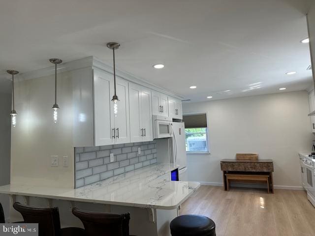 kitchen with hanging light fixtures, white cabinets, white appliances, kitchen peninsula, and a breakfast bar area