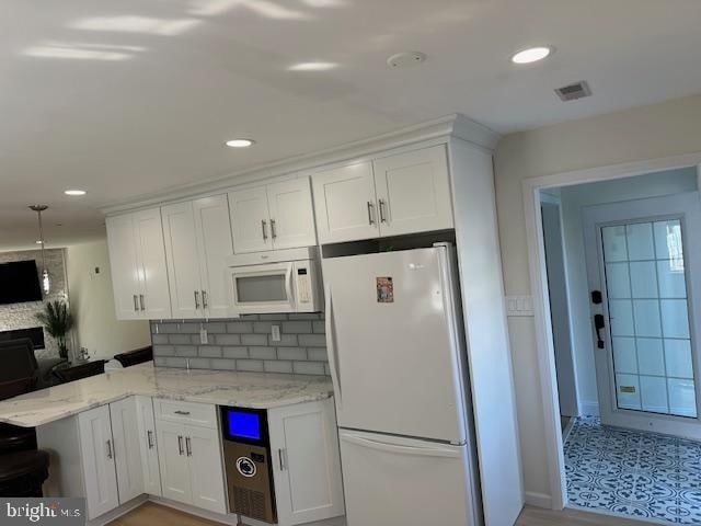 kitchen featuring light stone counters, white cabinetry, kitchen peninsula, white appliances, and backsplash