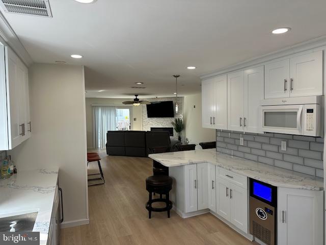 kitchen with ceiling fan, white cabinets, kitchen peninsula, a breakfast bar area, and light hardwood / wood-style floors