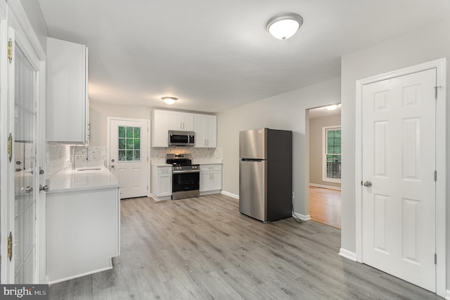 kitchen with backsplash, stainless steel appliances, sink, white cabinets, and plenty of natural light