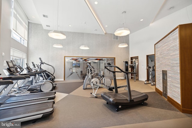 exercise room with light colored carpet and a towering ceiling