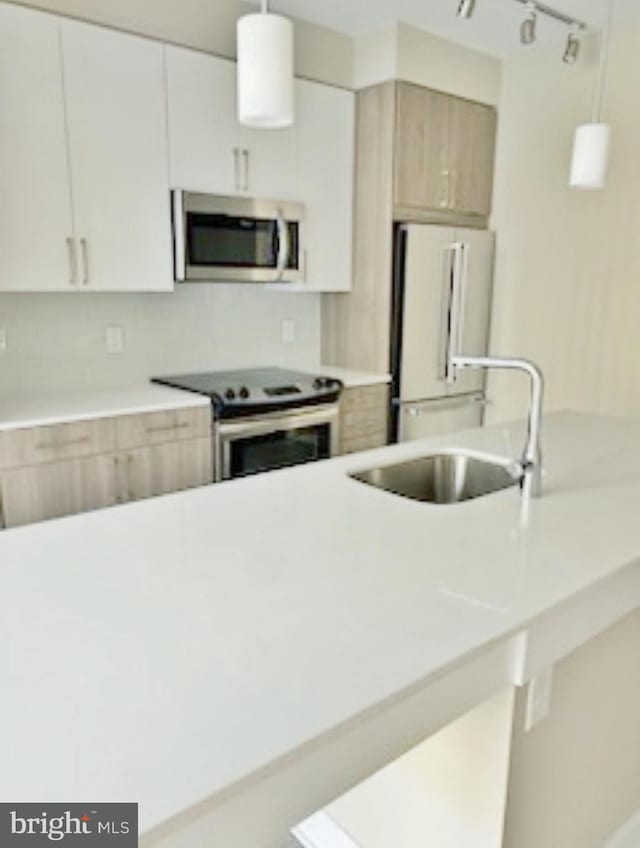 kitchen featuring white cabinets, light brown cabinetry, stainless steel appliances, sink, and pendant lighting