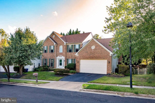 colonial home featuring aphalt driveway, a garage, brick siding, and a front yard