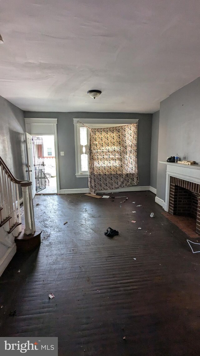 unfurnished living room with a brick fireplace and dark wood-type flooring