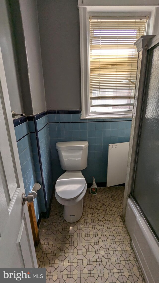 bathroom with tile walls, tile patterned flooring, shower / bath combination with glass door, and toilet