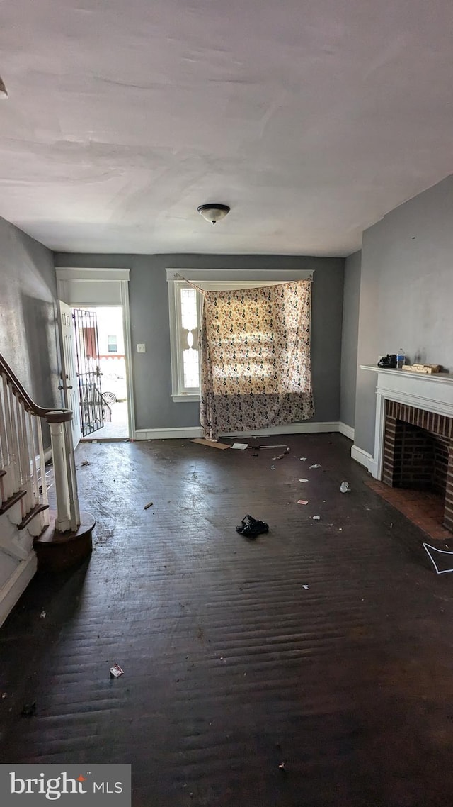 unfurnished living room featuring dark hardwood / wood-style floors and a brick fireplace