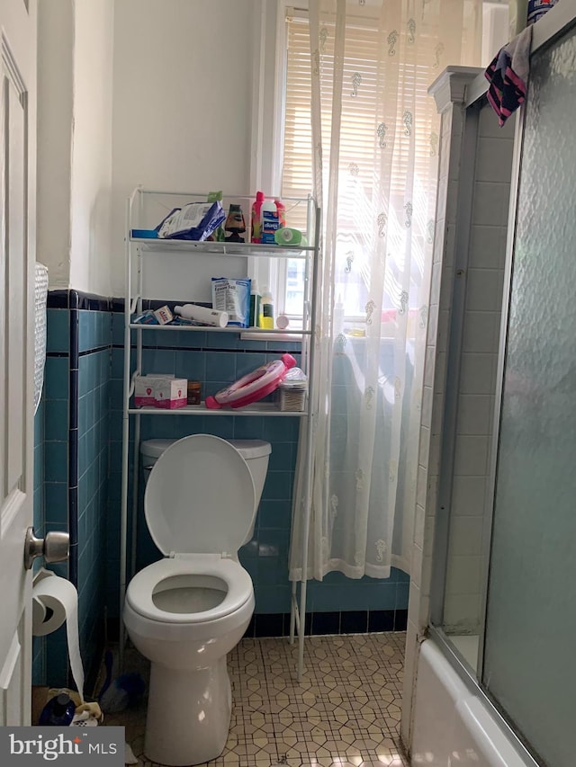 bathroom featuring tile walls, shower / bath combination with glass door, tile patterned floors, and toilet