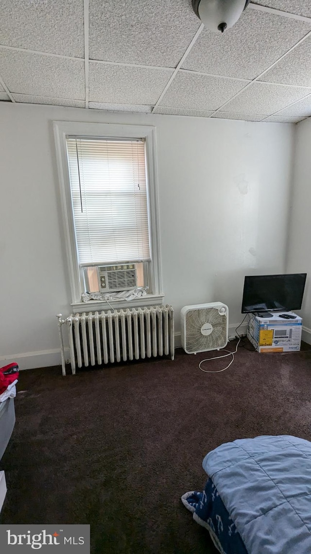 bedroom featuring a drop ceiling, dark colored carpet, and radiator heating unit