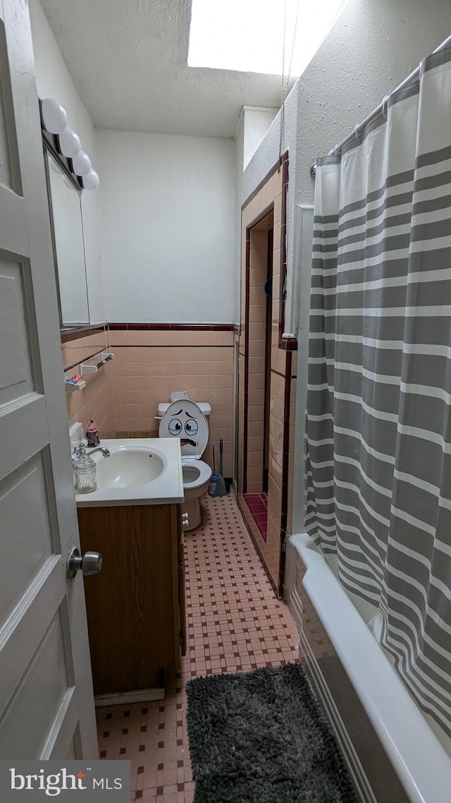 full bathroom with shower / bath combination with curtain, tile walls, a textured ceiling, vanity, and toilet