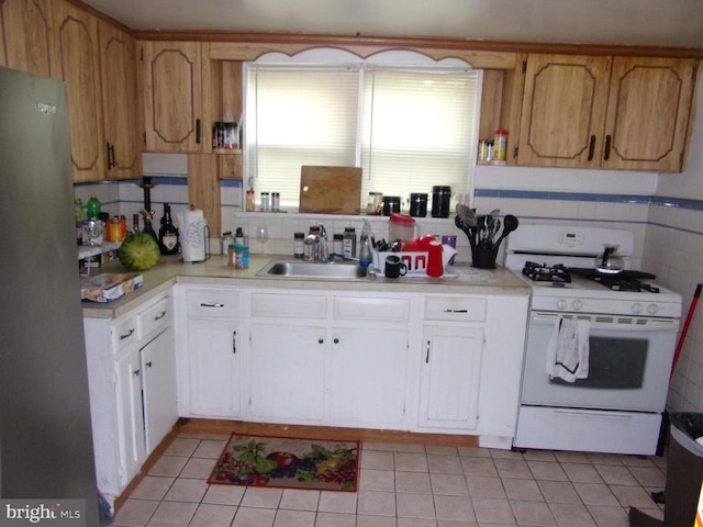 kitchen featuring white gas stove, tasteful backsplash, sink, white cabinetry, and stainless steel fridge