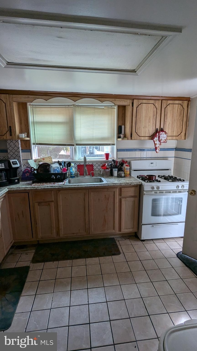 kitchen with backsplash, white gas range, light tile patterned flooring, and sink