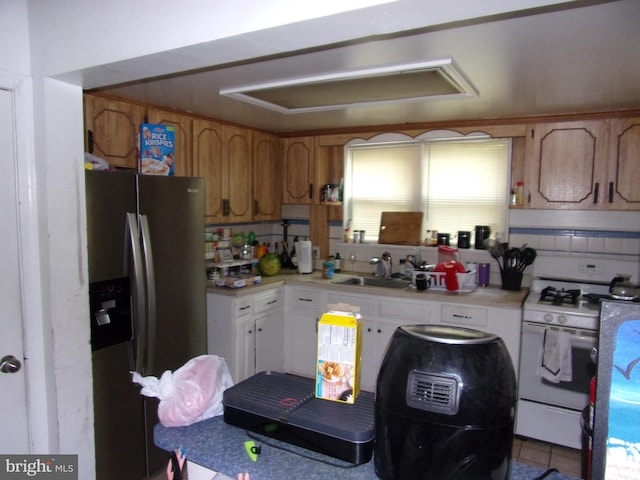 kitchen with light tile patterned flooring, stainless steel fridge with ice dispenser, sink, white cabinets, and white gas range