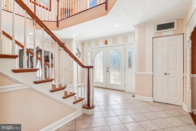 foyer entrance featuring crown molding, french doors, and light tile patterned floors