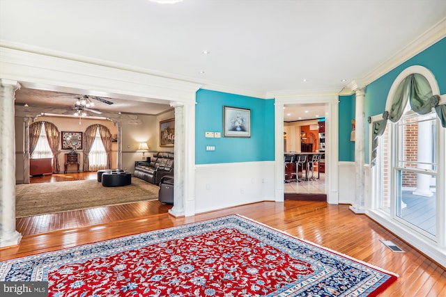 foyer entrance with ceiling fan, hardwood / wood-style flooring, ornate columns, and ornamental molding