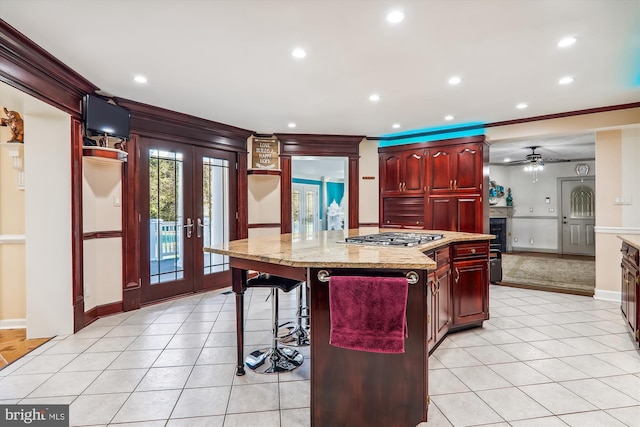 kitchen with light stone counters, stainless steel gas cooktop, french doors, a kitchen breakfast bar, and a center island