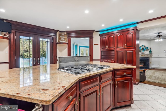 kitchen with light tile patterned flooring, stainless steel gas cooktop, light stone counters, and a center island