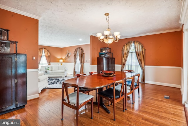 dining space featuring an inviting chandelier, a textured ceiling, light hardwood / wood-style flooring, and crown molding