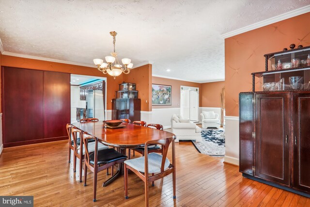 dining space featuring ornamental molding, an inviting chandelier, light wood-type flooring, and a textured ceiling