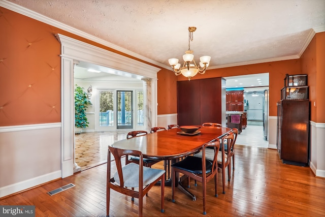 dining space featuring a chandelier, ornate columns, hardwood / wood-style floors, ornamental molding, and a textured ceiling